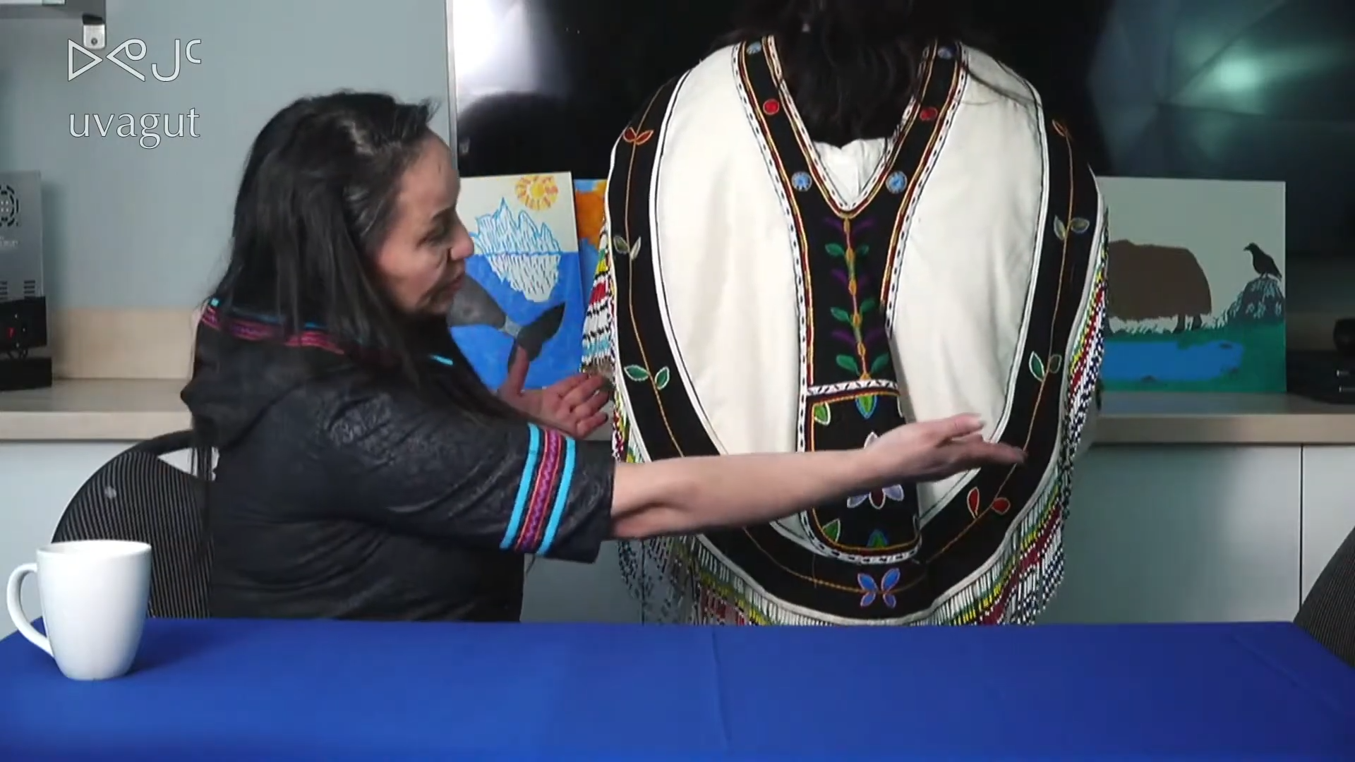 A woman, who is on the TV station, Uvagut, is showing her parka.